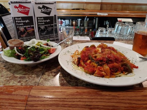 A plate of pasta with marinara sauce and a side salad on a table, with a glass of beer in the background.