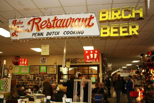 Interior of a bustling restaurant with a sign reading "Jake and Leon's Restaurant" and "Birch Beer" in bright lights.
