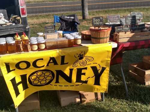 A market stall displaying jars of local honey, with a bright yellow banner reading "LOCAL HONEY" and various honey products.