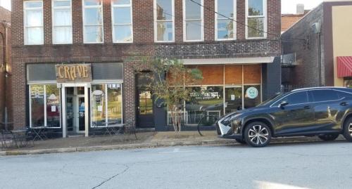 A brick building with a sign reading "Crave," featuring outdoor seating and a parked black SUV in front.