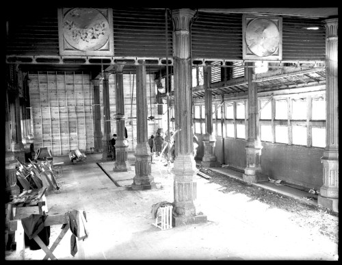 Black and white image of an empty industrial space with tall columns, large windows, and scattered tools.