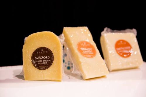 Three types of cheese displayed on a white surface, each with a label: Wexford, Braley, and another variety.