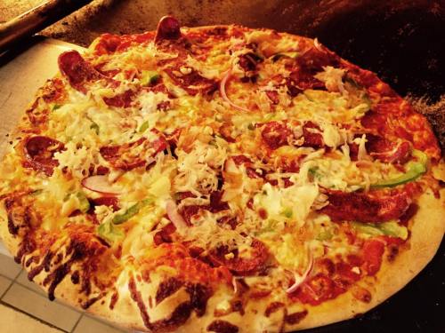 A freshly baked pizza topped with pepperoni, green peppers, onions, and melted cheese on a crispy crust.