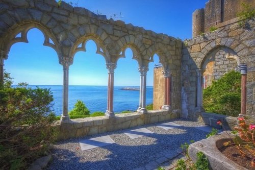 A stone archway overlooking a serene ocean view, framed by greenery and a clear blue sky.