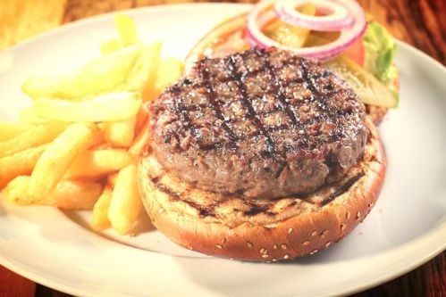 A juicy grilled burger patty on a sesame seed bun, served with crispy fries and fresh toppings.