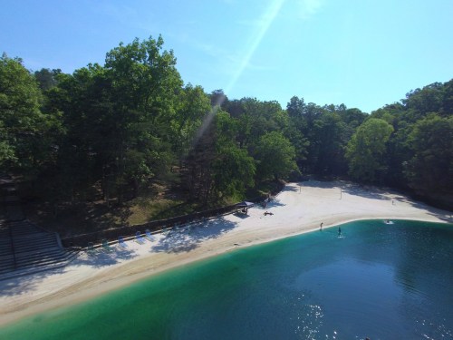 A serene beach with white sand and clear water, surrounded by lush green trees under a bright blue sky.