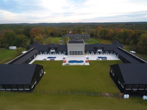 Aerial view of a modern building complex with pools, surrounded by green lawns and trees in the background.