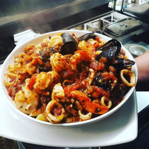 A bowl of seafood pasta with shrimp, mussels, and a rich tomato sauce, garnished with herbs.