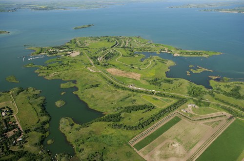 Aerial view of a lush green island surrounded by blue water, featuring winding roads and patches of farmland.
