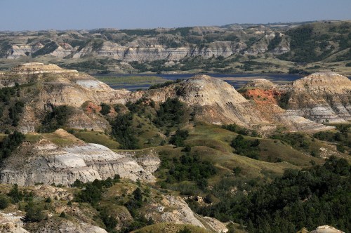 A panoramic view of rugged hills and valleys with layered rock formations and greenery under a clear blue sky.