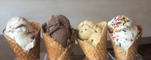 Four ice cream cones with different flavors: white with fruit, chocolate, yellow, and vanilla topped with sprinkles.
