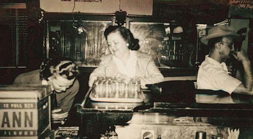 A vintage bar scene featuring two women at the counter and a man in a cowboy hat, with glassware and a Coca-Cola sign.