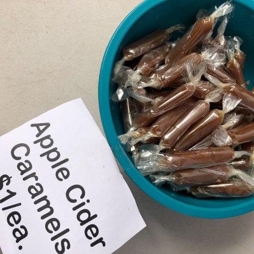 A turquoise bowl filled with individually wrapped apple cider caramels, next to a sign listing the price as $1 each.