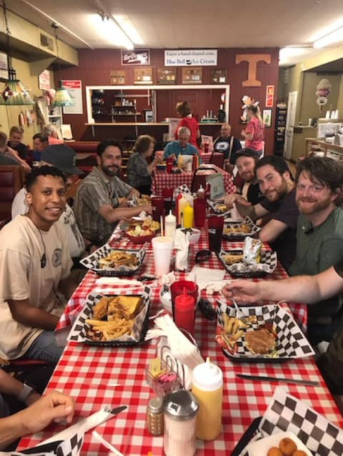 A group of people enjoying a meal at a diner, seated at a table with checkered tablecloths and various food items.