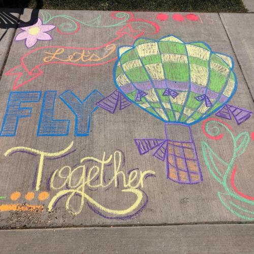 Colorful chalk drawing on pavement featuring a hot air balloon and the text "Let's Fly Together."