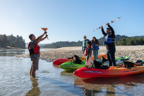 A group of people in kayaks on a river, with one person holding a fish while others cheer and raise paddles.