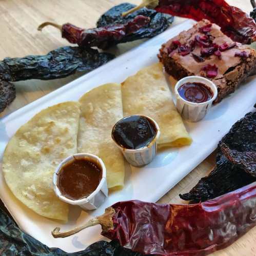 A plate with three tortillas, two sauces, and a brownie, surrounded by dried red chilies.