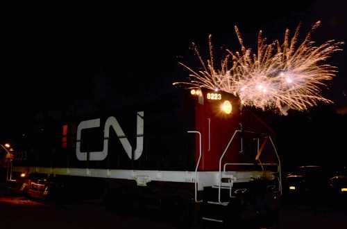 A CN train at night with colorful fireworks exploding in the background.