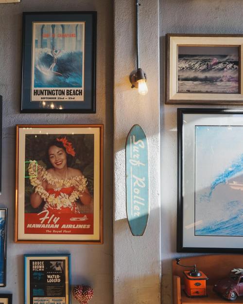A wall adorned with vintage posters, a surfboard, and a framed photo of a woman in a floral lei.