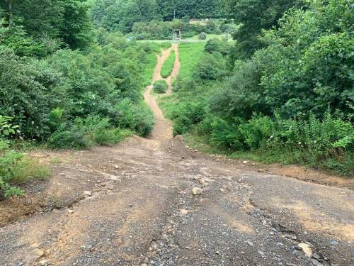 A steep, rocky path leads down through lush greenery, with winding trails visible in the distance.
