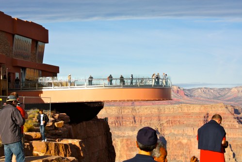Visitors on a glass observation deck at the Grand Canyon, with stunning rock formations in the background.