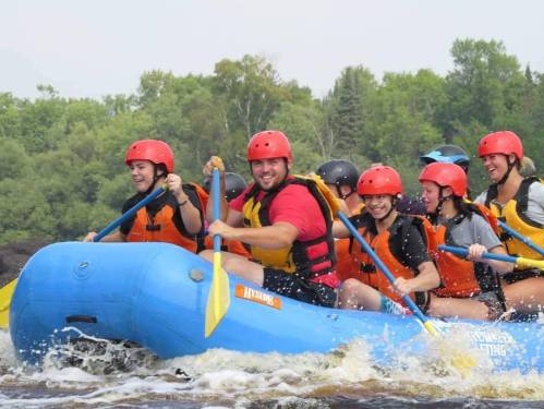 A group of people in red helmets and life jackets enjoying white-water rafting on a river.