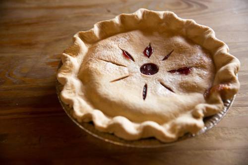 A freshly baked pie with a decorative crust and fruit filling, placed on a wooden table.