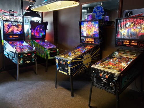 A row of colorful pinball machines in a dimly lit arcade, featuring various themes and vibrant lights.