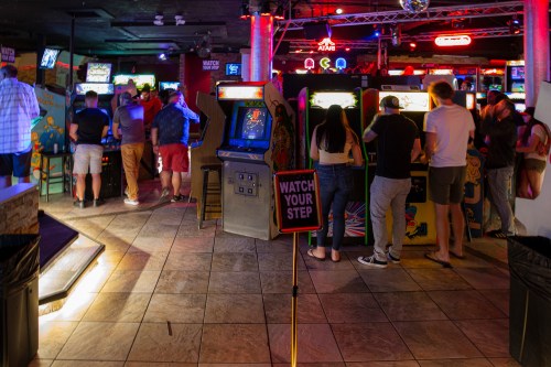 A lively arcade scene with people playing vintage games and neon lights illuminating the space.