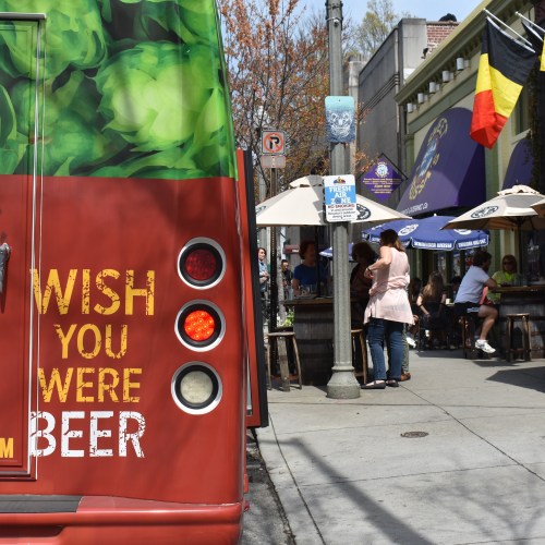 A food truck with "WISH YOU WERE BEER" on the side, near outdoor seating and people enjoying a sunny day.