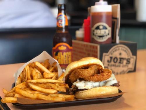 A plate featuring a burger with onion rings, melted cheese, fries, and a bottle of soda in the background.