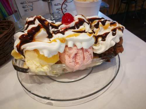 A colorful ice cream sundae with three scoops, whipped cream, chocolate sauce, and a cherry on top.