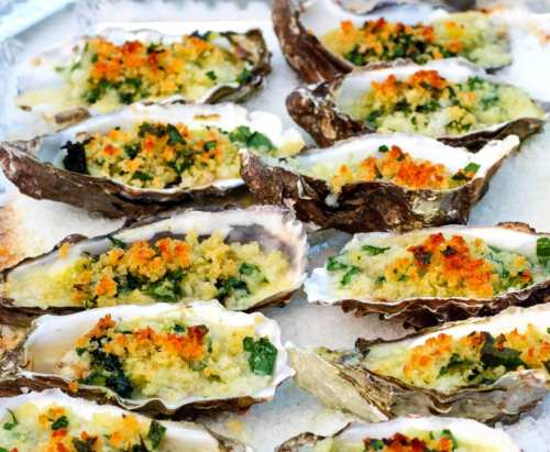Baked oysters topped with a golden breadcrumb and herb mixture, arranged on a platter.