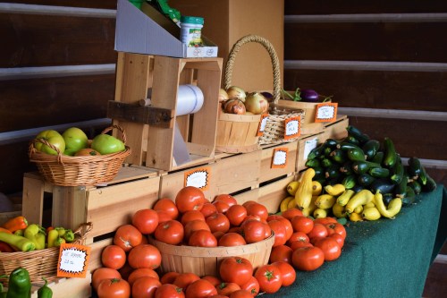 A wooden display of fresh vegetables and fruits, including tomatoes, zucchini, apples, and bananas, in a rustic setting.