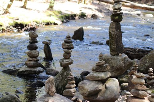 A serene stream with several stacked stone cairns along the water's edge, surrounded by greenery.