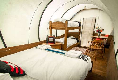 Cozy interior of a glamping tent featuring bunk beds, a double bed, a small table, and decorative elements.