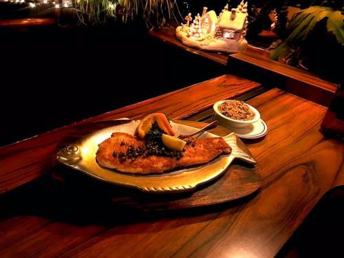 A beautifully plated fish dish with lemon and greens, served on a wooden table with a side of rice.