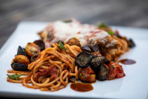 A plate of spaghetti with marinara sauce, roasted vegetables, and a cheesy baked dish, garnished with herbs.