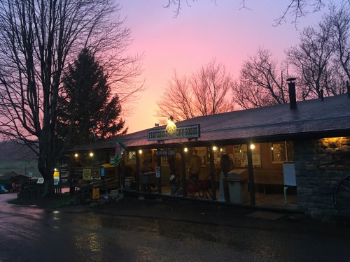 A rustic store with a stone facade, illuminated by a colorful sunset sky, surrounded by bare trees.