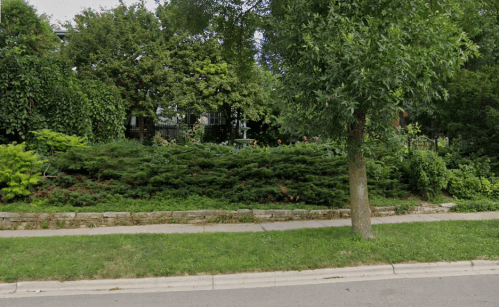 Lush green garden with shrubs and trees along a sidewalk, creating a serene outdoor space.
