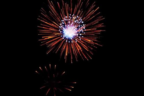 Colorful fireworks burst against a dark sky, creating vibrant patterns of light in shades of orange, blue, and white.