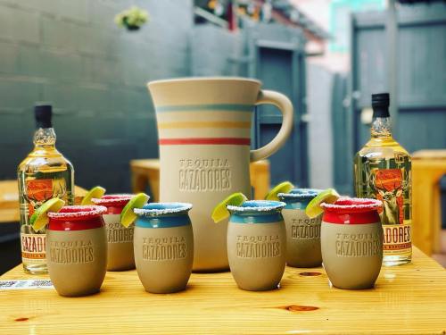 A pitcher and several small cups of tequila, garnished with lime, arranged on a wooden table.