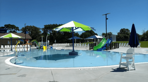 A sunny pool area featuring colorful slides, umbrellas, and lounge chairs, with a clear blue sky above.