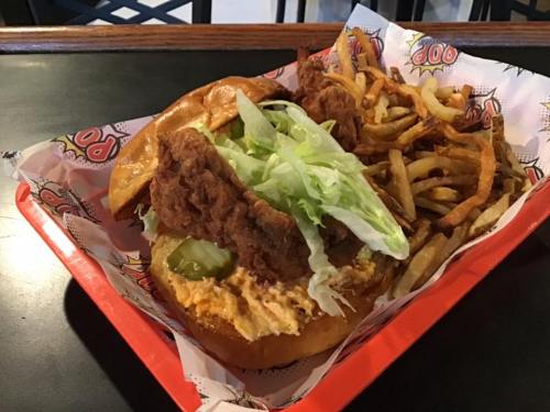 A crispy chicken sandwich with lettuce and pickles, served with a side of golden French fries on a red tray.