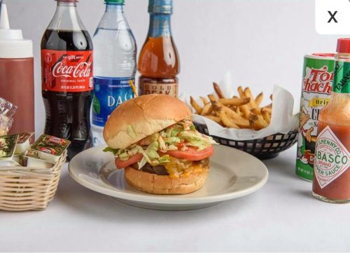 A burger with lettuce and tomato on a plate, surrounded by drinks, fries, and condiments.