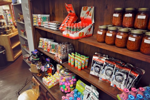 A wooden shelf filled with various snacks, sauces, and candies in jars and packages, creating a colorful display.