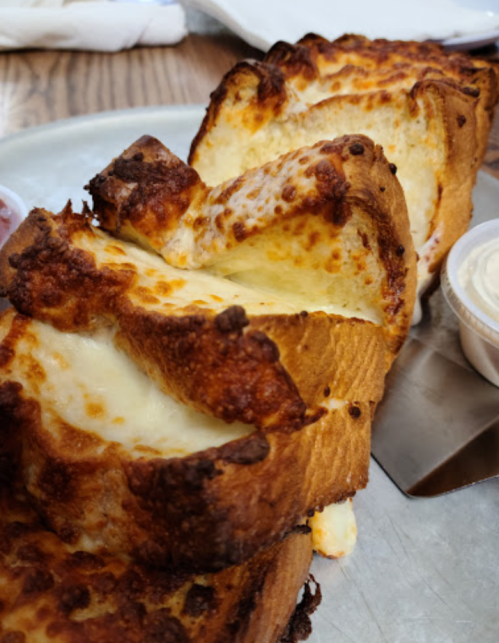 A close-up of toasted bread slices with melted cheese, served on a metal tray with dipping sauces.