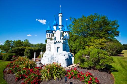 A whimsical castle with blue turrets surrounded by colorful flowers and lush greenery under a clear blue sky.