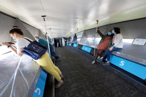 People wearing masks inside a bus, some looking out the windows, with numbered seats visible along the walls.
