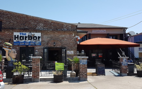 A brick building with a sign for "The Harbor," featuring outdoor seating and an orange umbrella on a sunny day.